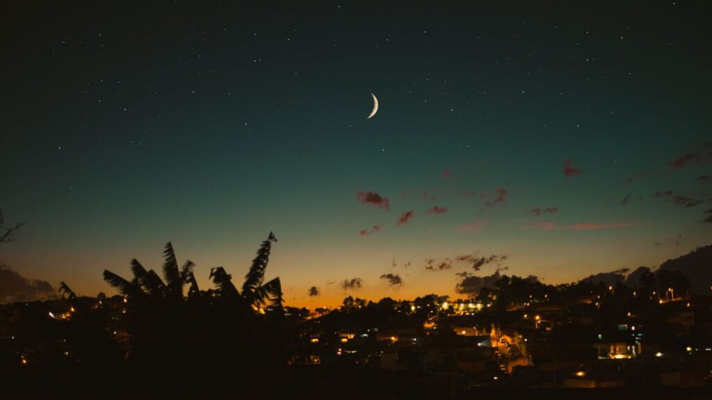 夕焼けの残る空に三日月が浮かび、街の明かりが灯る夜景