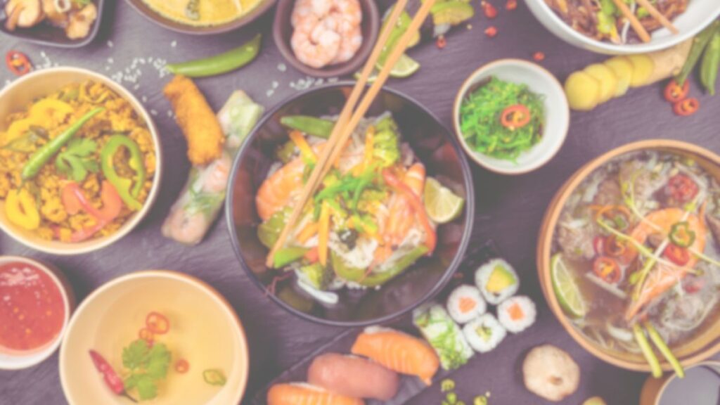 たくさんのアジア料理がテーブルいっぱいに並んでいる。寿司、チャーハン、麺類など、様々な料理がカラフルで賑やかな雰囲気を作っている。