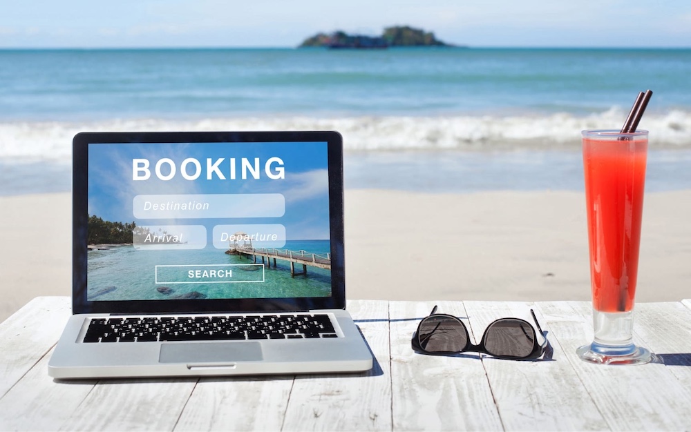 海辺のテーブルでパソコンから旅行予約をするイメージ。石垣島ディナークルーズも公式サイトから簡単に予約可能