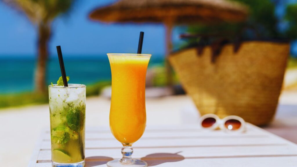 海辺のカフェで楽しむカクテルとフレッシュジュース。青い海を背景にリゾート気分を味わえるひととき